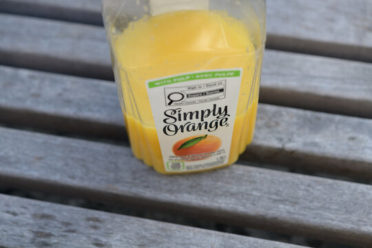 discarded half drunk plastic bottle of "Simply Orange" (Coca-Cola) on a wooden bench in Toronto