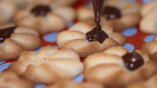 Close-up of freshly baked cookies arranged on a colorful baking mat as chocolate is drizzled on top, showcasing the delicious decoration process and the inviting texture of the treats