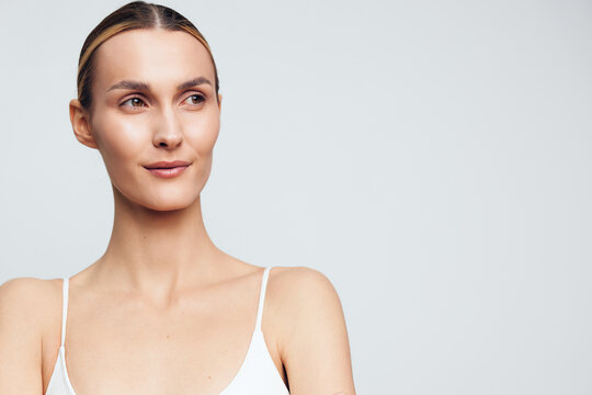 Woman portrait with clear skin and natural makeup in a studio, neutral background, soft lighting, calm expression, minimal styling, clean composition, conveying wellness and beauty