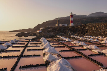 Montículos de sal marina y estanques rosados en primer plano con el faro de Fuencaliente y la costa volcánica de La Palma al atardecer. © Maxi Perez