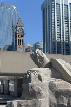 stone turtle "The Restoration of Identity" by Solomon King at the Spirit Garden in Nathan Phillips Square with clocktower of Old City Hall, Toronto