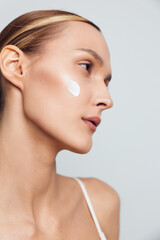 Close profile of a young woman applying sunscreen on her cheek in a studio with soft lighting, calm expression, and natural skin glow. © SHOTPRIME STUDIO