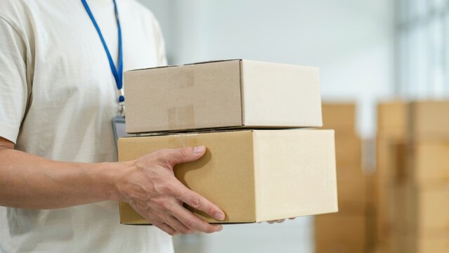 Courier holding two cardboard parcel boxes in warehouse setting