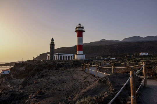 Los faros de Fuencaliente, el antiguo de piedra y el moderno de franjas rojas y blancas, sobre la costa volc&aacute;nica de La Palma a la luz del atardecer.