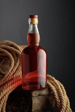 Bottle of whiskey on a rough wooden crate with hay, next to a natural hemp rope.