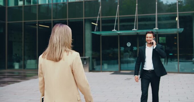 Two colleagues of adult man and young woman, walk toward each other outside a modern office building, smiling cheerfully, exchanging a high five, then parting ways to continue their day