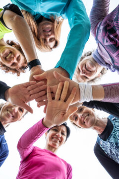 Generation x and baby boomer women stack hands in a low-angle fitness huddle. Energetic outdoor group expresses teamwork, unity, motivation, active aging, and female solidarity.