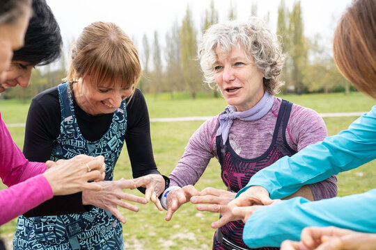 Mature women gather in a fitness circle before outdoor exercise. Generation x and baby boomer friends share motivation, teamwork, laughter, and active aging in a park.