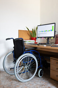 Wheelchair at a desk with a computer monitor displaying business graphs, suggesting remote work and disability