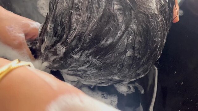 Hairstylist washing soapy dark hair with foam in salon basin for hair care and treatment banner, horizontal