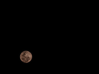 Stunning full moon glowing in a pure black night sky. Detailed lunar craters with a warm pinkish tint © MuhammadRizki