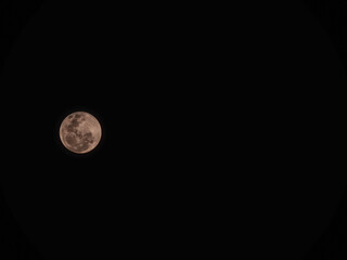 Stunning full moon glowing in a pure black night sky. Detailed lunar craters with a warm pinkish tint © MuhammadRizki