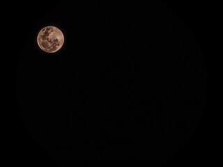 Stunning full moon glowing in a pure black night sky. Detailed lunar craters with a warm pinkish tint © MuhammadRizki