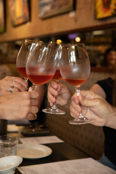 four hands toasting with glass of wine in a bistro