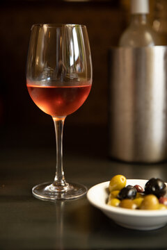 bottle of chilled rose in a metal wine cooler at a restaurant table with glass of rose and side of olives