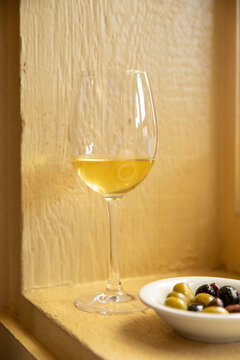 vertical shot of white wine in a glass and bowl of mixed olives in front of yellow wall