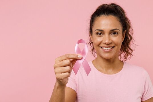 Mulher brasileira sorridente segurando la&ccedil;o rosa contra fundo rosa pastel. Campanha de conscientiza&ccedil;&atilde;o do c&acirc;ncer de mama e sa&uacute;de feminina no Outubro Rosa. Espa&ccedil;o para texto.