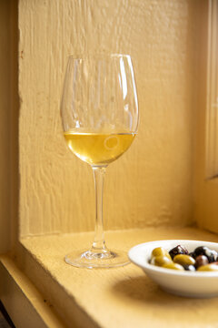 vertical shot of white wine in a glass and bowl of mixed olives in front of yellow wall