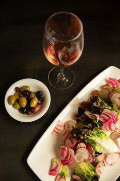 overhead shot of lettuce and radish salad with side of mixed olives and wine