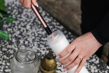 Woman lighting memorial candle at cemetery background. Electric lighter ignites wick inside...