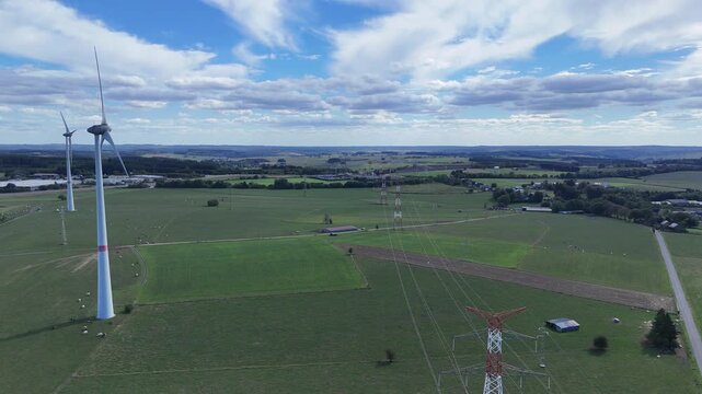 survol en drone des champs agricoles pr&egrave;s de Bastogne, entre les &eacute;oliennes et les lignes &eacute;lectriques haute tension . Les pyl&ocirc;nes blancs et rouges supportent les c&acirc;bles et &eacute;gayent le paysage rural 
