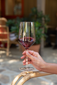 female hand holding a wine glass receiving a pour of red wine at an outdoor winery, resting hand on a rattan arm chair