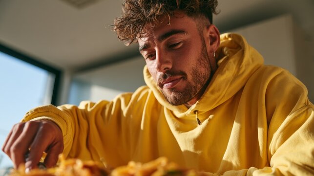 Young Man in Yellow Sweatshirt Eating a Snack, Looking Down and Out of Focus
