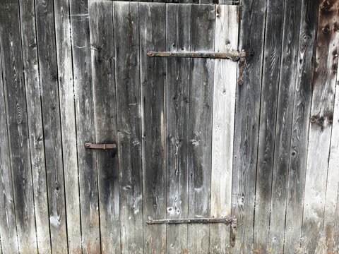 Weathered old wooden barn door with rusty strap hinges texture