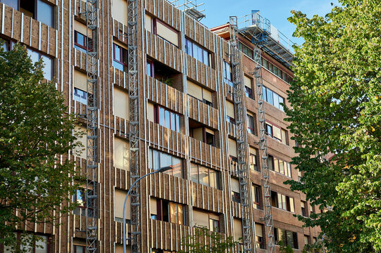 angled view of renovated building facade with wood-effect insulation cladding and trees