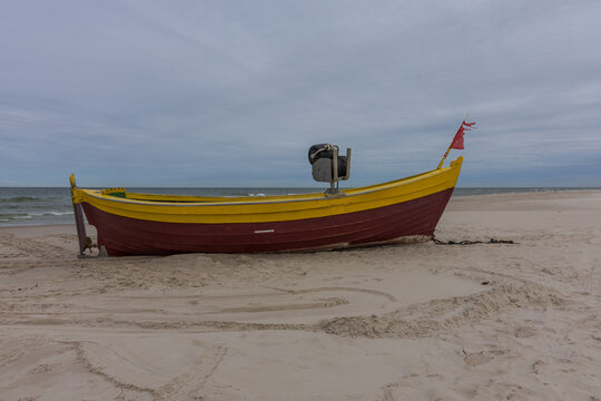 Traditional yellow and red wooden fishing boat resting on sandy Baltic Sea beach