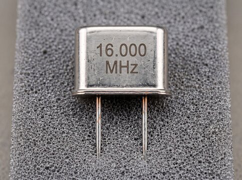 Silver metallic quartz crystal oscillator unit resting on textured grey foam packaging.