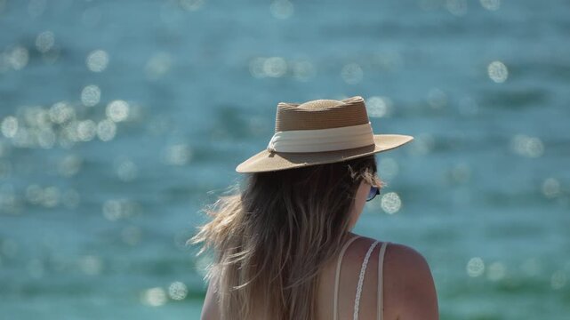 Woman gazing out over sparkling sea waves while standing at the tropical coast. Static close-up shot.
