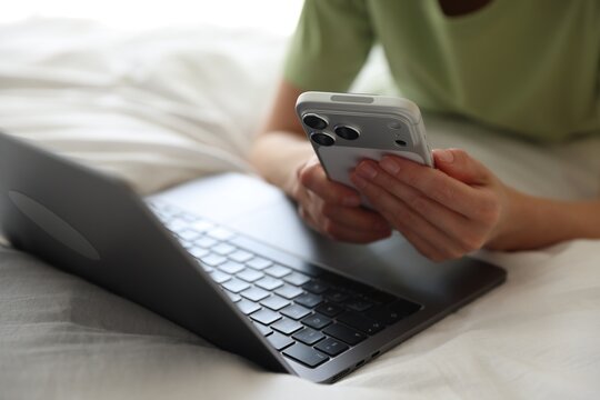 Woman with laptop and smartphone in bed at home, closeup