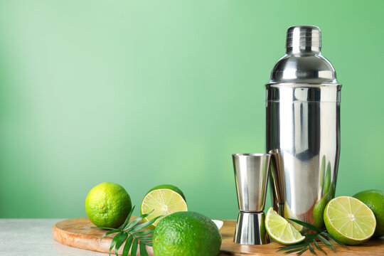 Limes, shaker, jigger and leaves on light grey table. Space for text