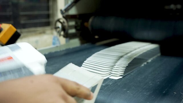 Worker Inspecting Printed Booklets on Conveyor Belt