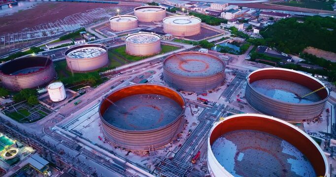 Aerial view of large cylindrical storage tanks at an industrial chemical facility with connecting pipelines, captured under bright sunlight.