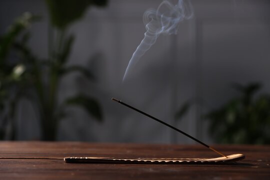 Smoldering incense stick on wooden table indoors, closeup