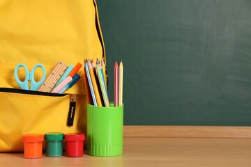 Backpack with stationery on wooden table against chalkboard. Space for text © New Africa