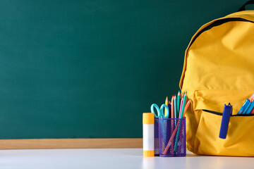 Backpack with stationery on white desk against chalkboard. Space for text © New Africa