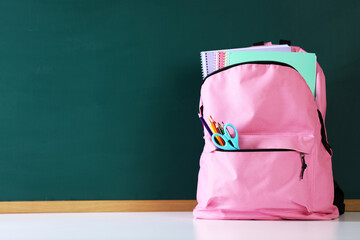 Backpack with notebooks and stationery on white desk against chalkboard. Space for text © New Africa