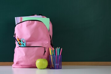 Backpack with stationery and apple on white desk against chalkboard. Space for text © New Africa