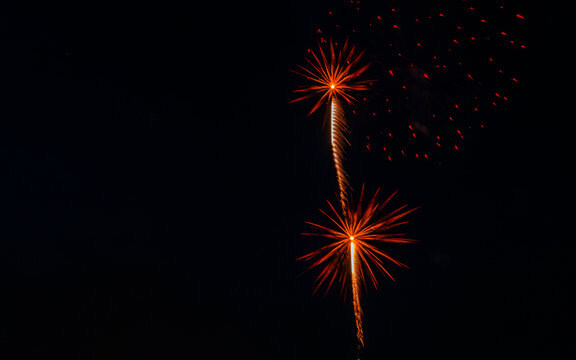 Fireworks burst in the night sky, displaying bright colors and patterns above the city. The event occurs during a lively celebration that attracts many spectators.