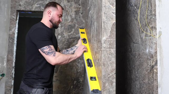 Construction worker using spirit level installing marble tile on wall