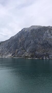 Majestic Rocky Mountain Cliff Rising Steeply from Calm Alaskan Ocean Inlet