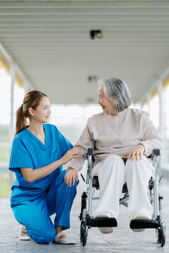 Kind nurse comforting senior patient sitting in wheelchair feeling happy and supported during medical visit in hospital corridor