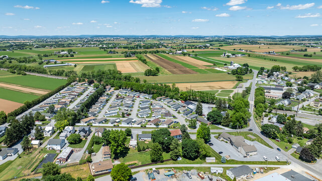 Aerial view shows fields and Mobile, Manufactured homes in a rural area. There are green and brown fields alongside a small neighborhood. The scene captures the layout of roads and houses.