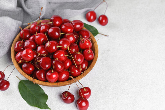 Fresh ripe sweet cherries in rustic wooden bowl with green leaves on light textured background. Top view flat lay with copy space. Juicy organic summer fruit, red berries, healthy seasonal food