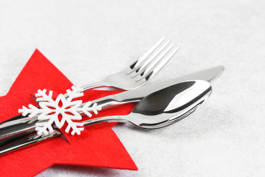 Christmas table setting with shiny silver cutlery arranged on a red star felt holder decorated with white snowflake on gray background. Festive holiday dining atmosphere.
