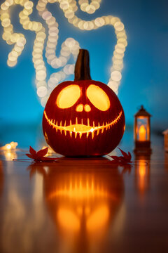 Single glowing Halloween jack-o'-lantern pumpkin with creepy toothy grin, beautiful autumn decoration with teal blue background, warm fairy light bokeh, and reflection