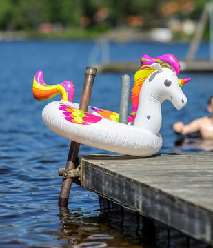 Colorful inflatable unicorn float resting on sunny lakeside dock.